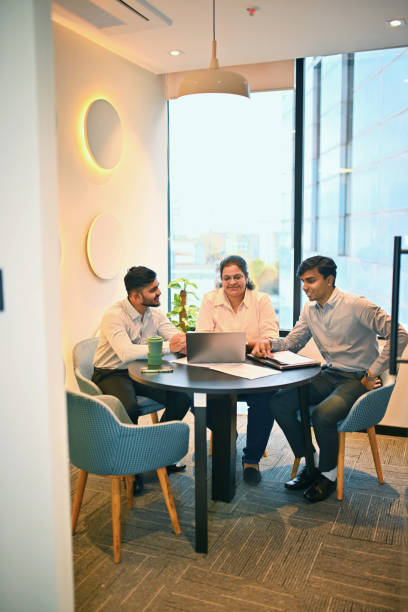 Three colleagues in a meeting with a laptop by floor-to-ceiling windows